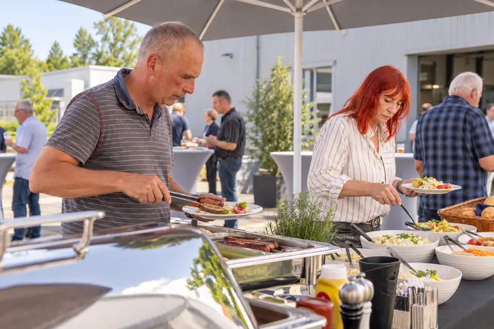 Beim Sommerfest holen sich zwei Kollegen am Buffet vor dem Werk etwas zu essen