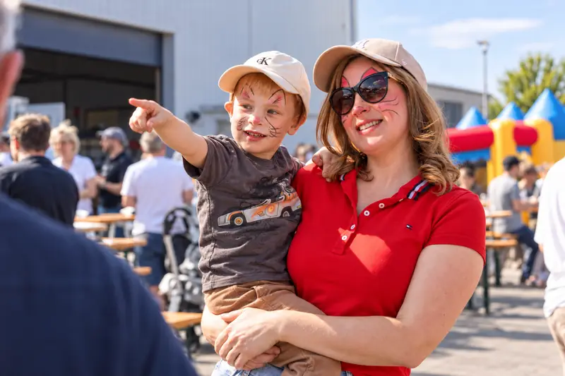 Eine Mutter mit Kind auf dem Arm beim Sommerfest, beide mit Gesichtsbemalung
