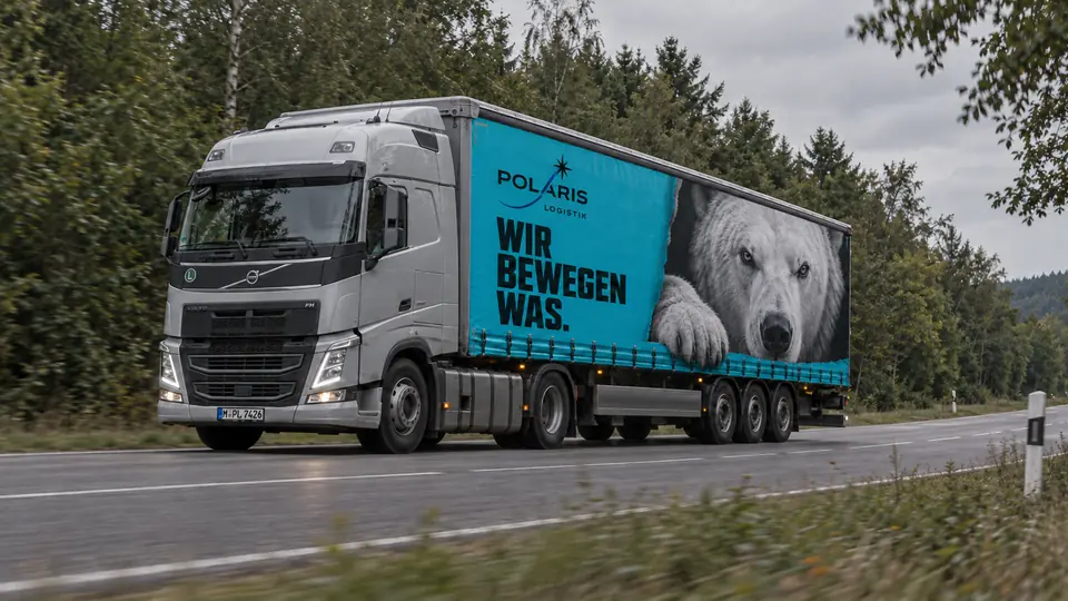 Ein Polaris-Lkw mit türkisem Auflieger und Eisbär-Motiv fährt auf einer Landstraße